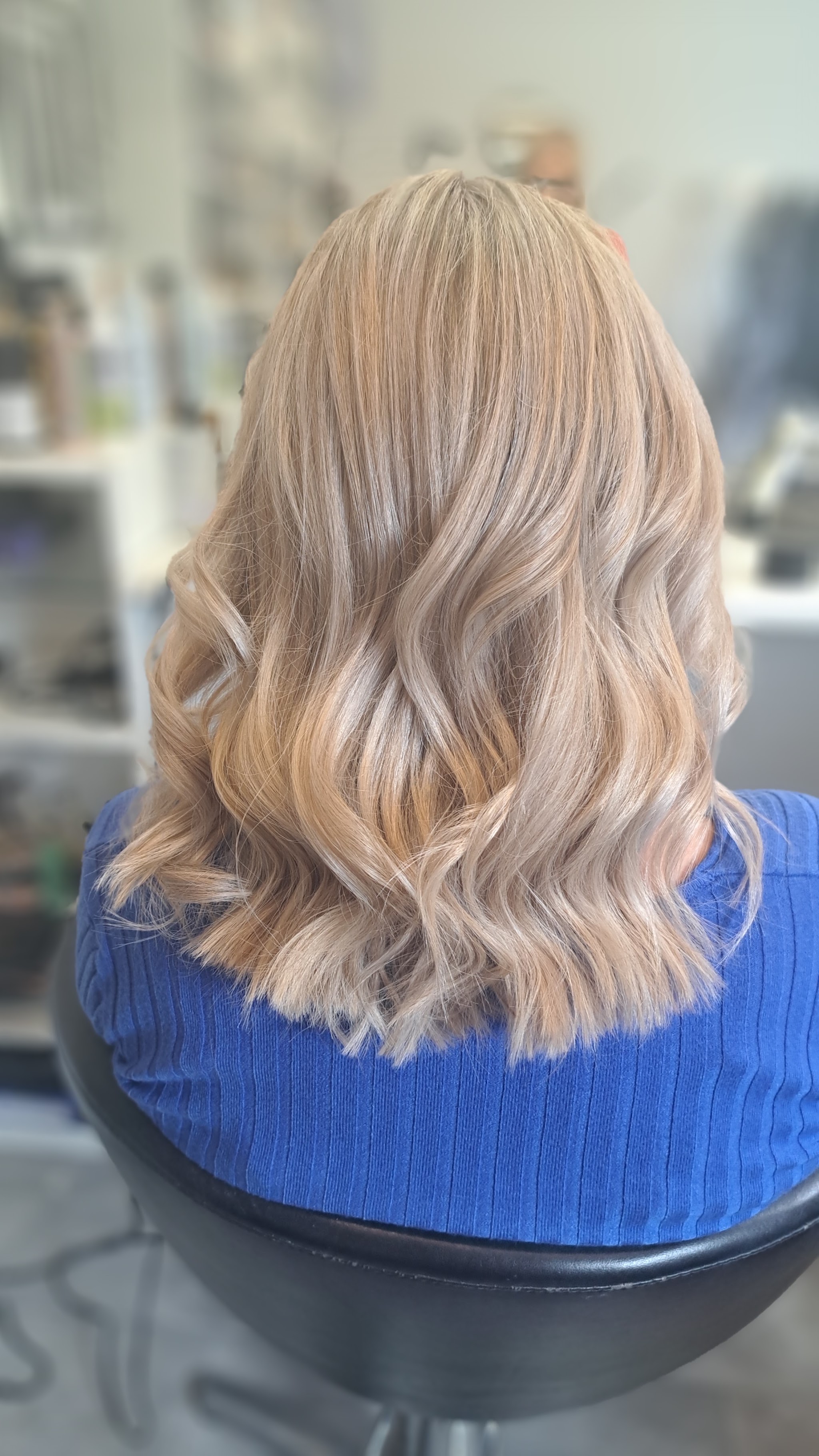 Lichtblond haar in zachte golven, van achteren, op een kappersstoel